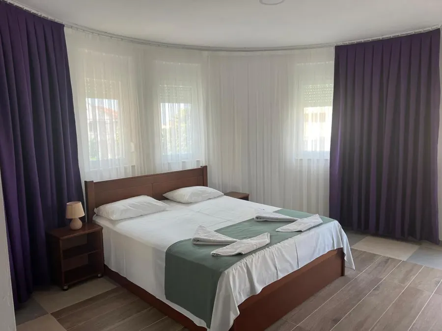 Double bed with white linen and purple curtains